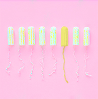 Eight tampons outside of their applicator sit in a row against a pink background and one is yellow.