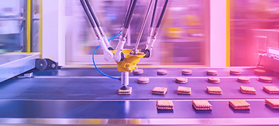 A manufacturing machine grabs a processed cookie sandwich from a conveyer belt.