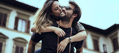 A man is giving a piggyback ride to a woman who is kissing his cheek.