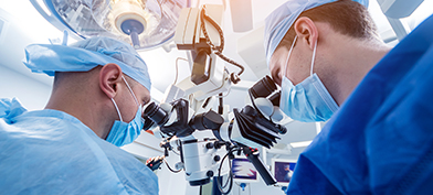 Two doctors look into a microsurgical machine during surgery.