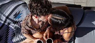 A man and and woman kiss while sitting down with cups of coffee in their hands.