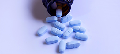 Blue pills spill out of a brown bottle onto a light blue surface.