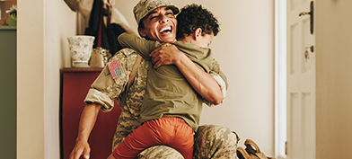 A uniformed army mom smiles as she crouches down to hug her child.