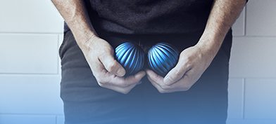 A man holds one blue ball in each hand cupped down near his groin. 
