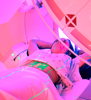A woman lies down under a radiation machine.