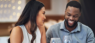 A man and woman are smiling as they talk and drink wine on a date.