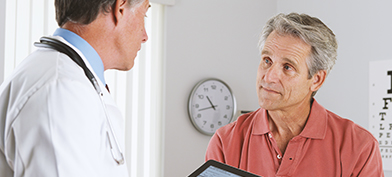A male patient sits in front of a doctor with a tablet during a health screening.