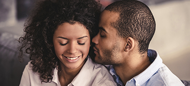 A woman closes her eyes and smiles while her partner puts his face close to her ear.