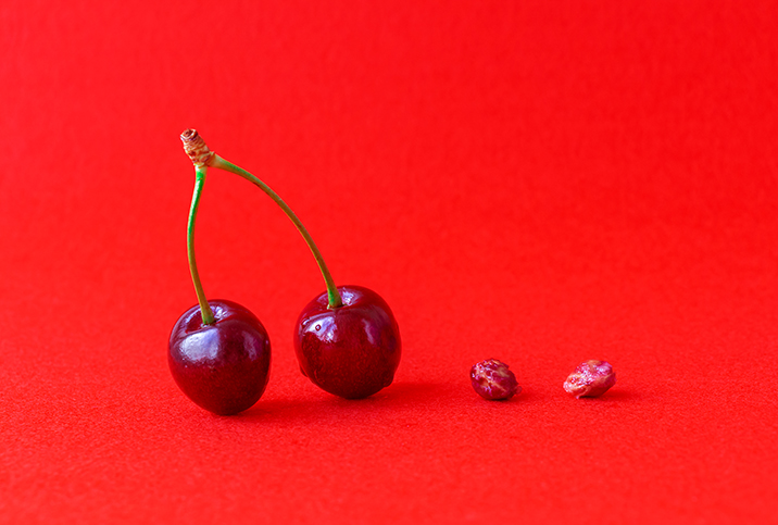 A pair of cherries on stems is on the left and a pair of cherry pits is on the right.