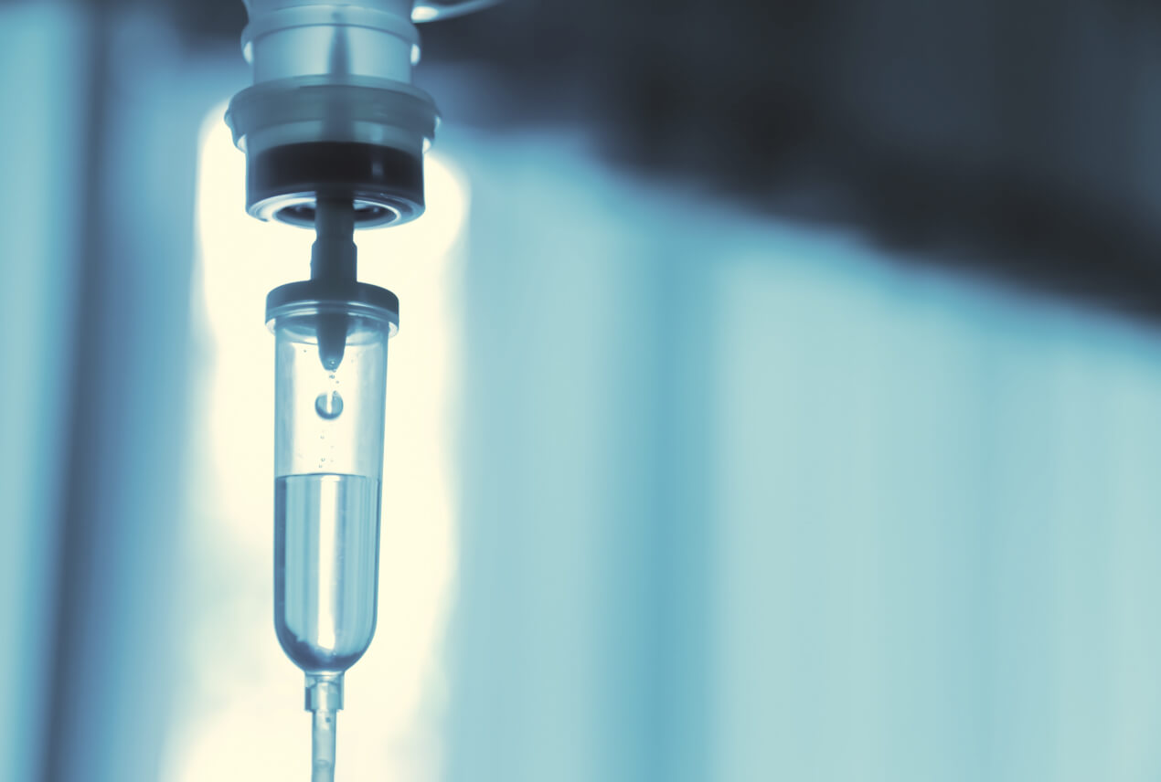 An IV drip hangs near a window with the sun shining through it.