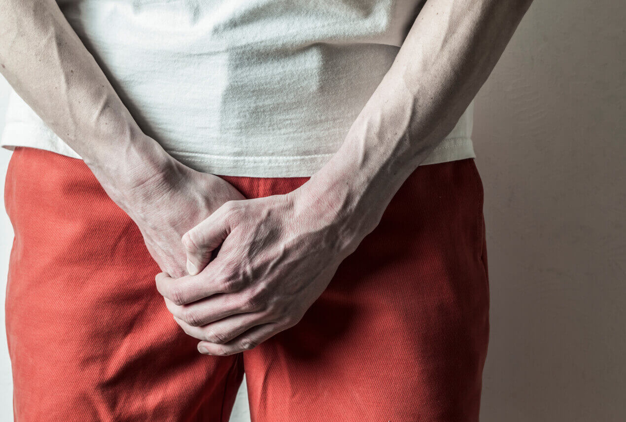 A person holds their hands together down above their groin.