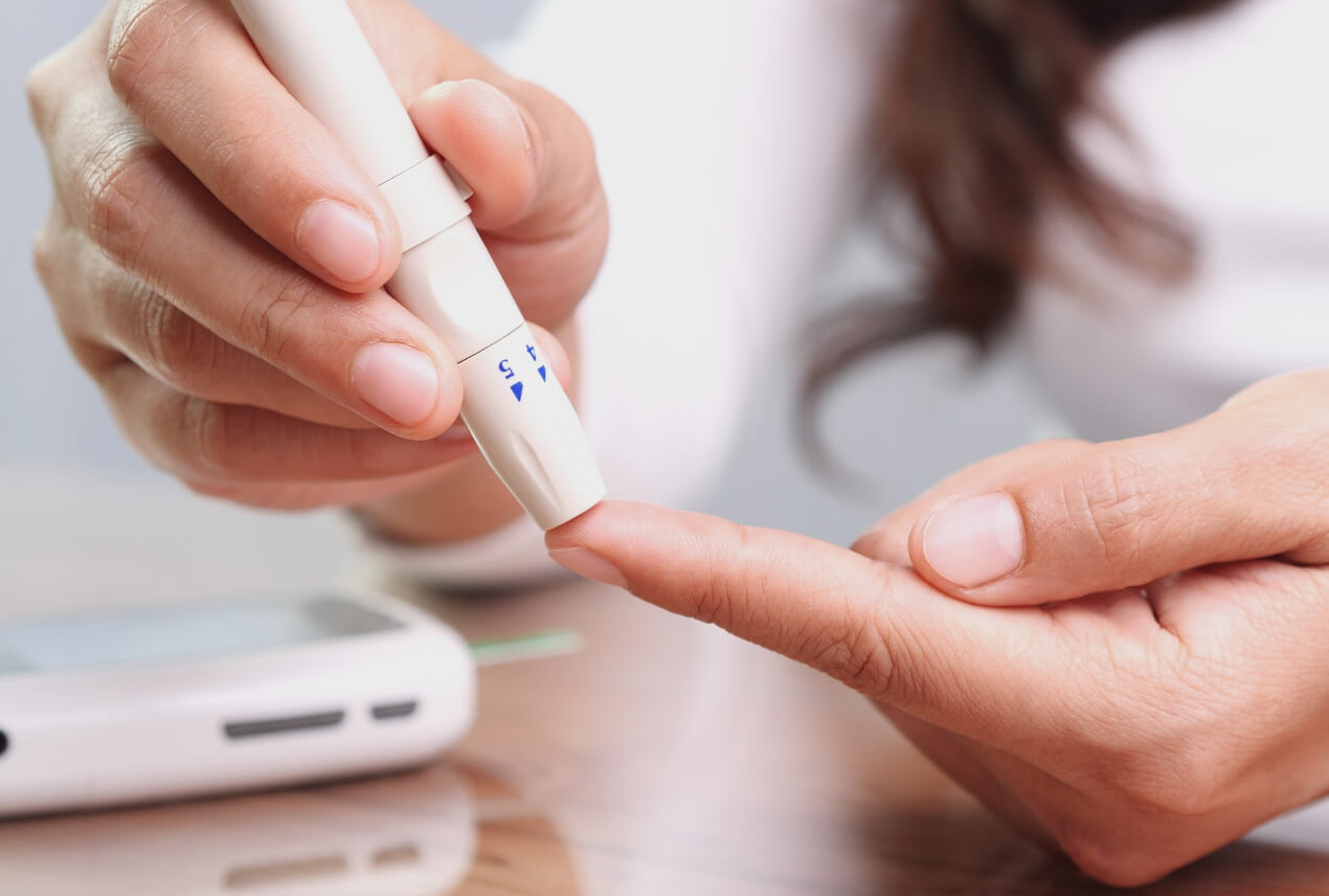 A person holds a lancing device to their finger tip to test their blood sugar.