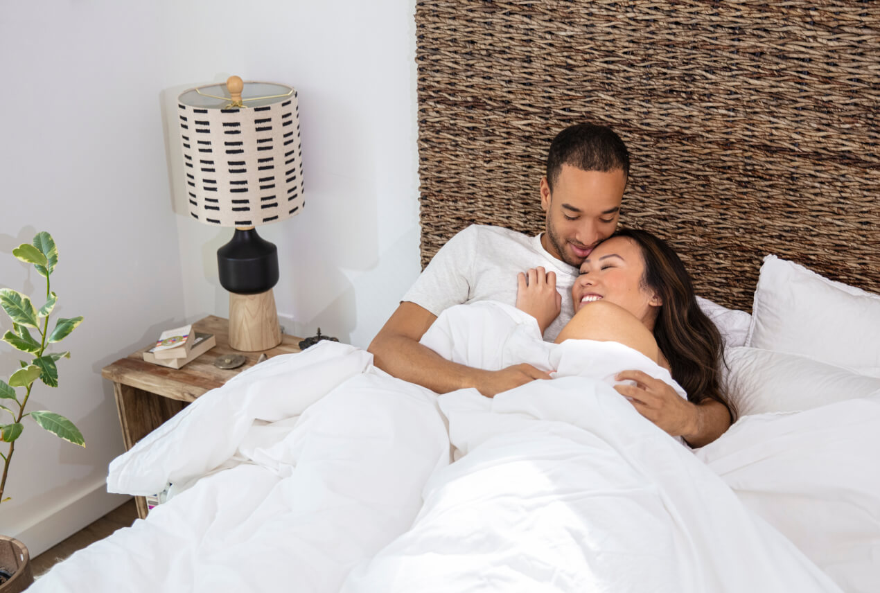 A couple cuddles in a bed with white sheets.