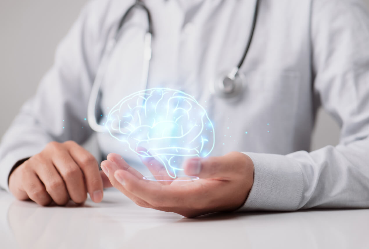 A doctor sits with his arms on a table and a glowing diagram of the human brain in his left palm.