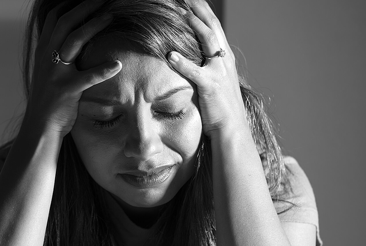 An upset woman holds her head in her hands.