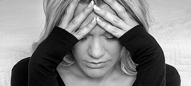 A black and white photo shows a distressed woman wither her forehead in her hands.