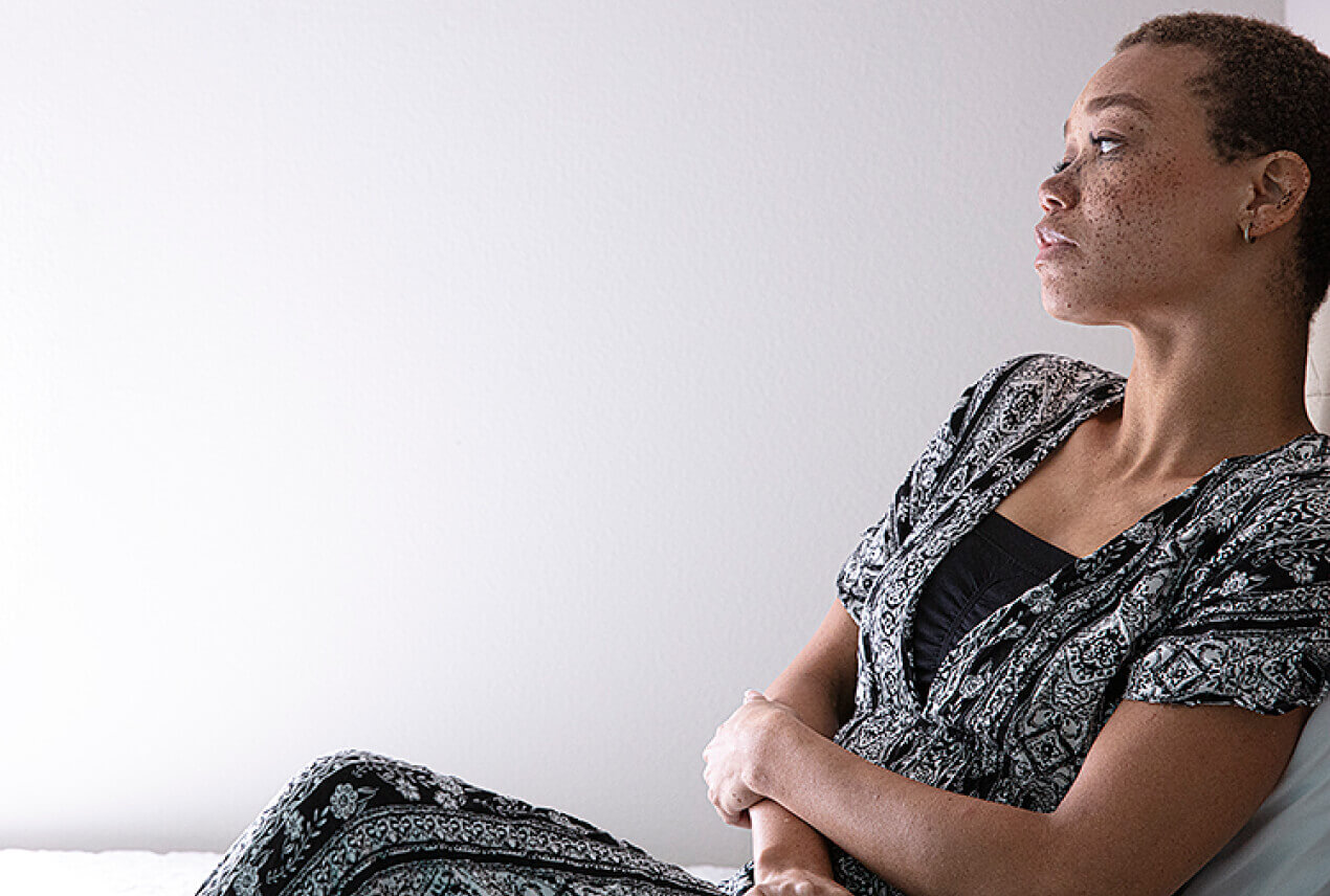 A woman sits leaning against a white wall as she looks off to the side.