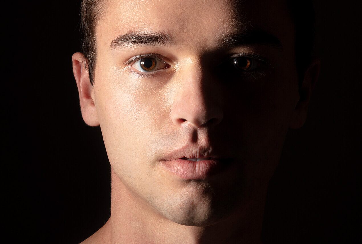 A man looks directly at the camera and half his face is in shadows.