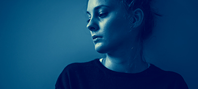 A woman looks down and to the side with a blue tint over the photo.