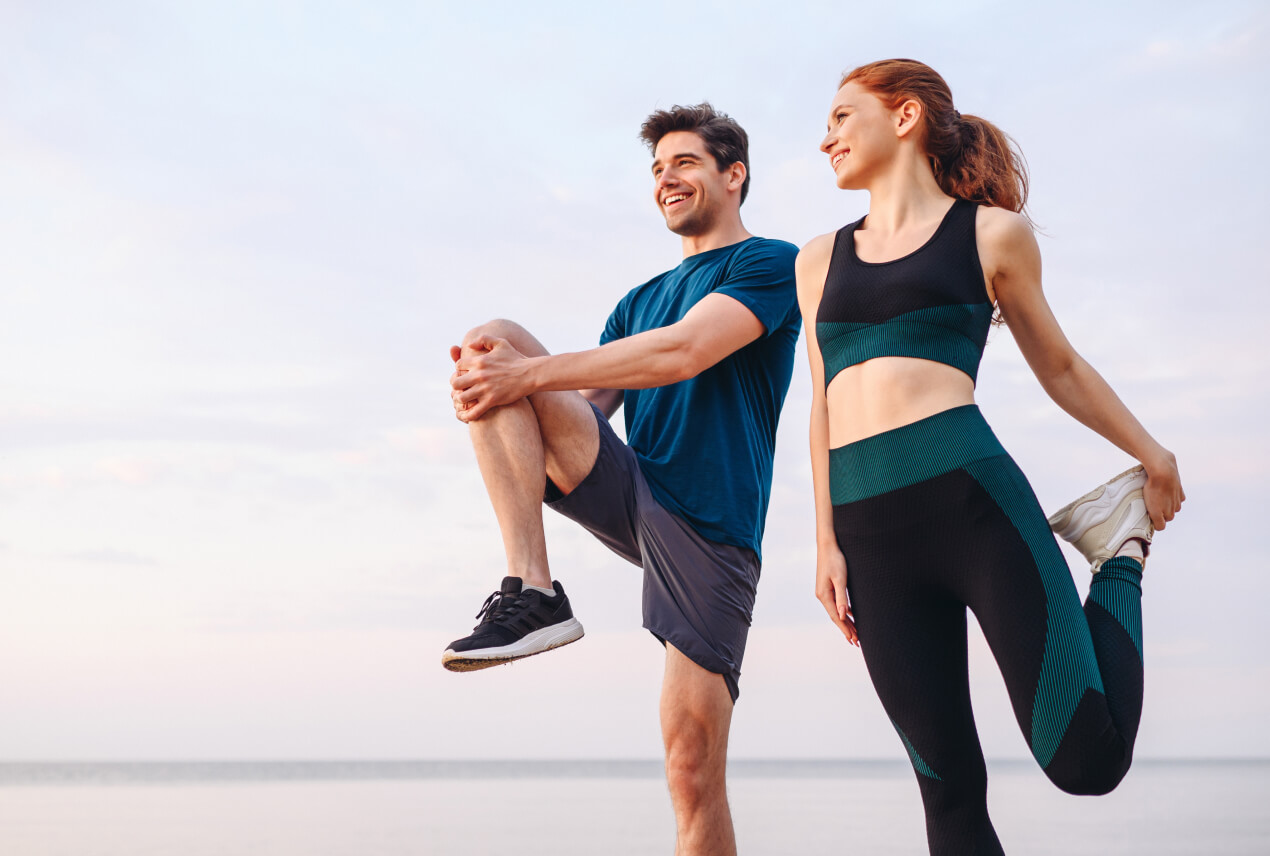A man and woman stand, stretching, with the sky behind them.
