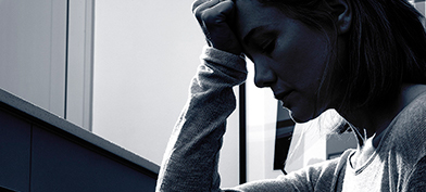 A black and white photo shows the profile of a person with their head in their hand.