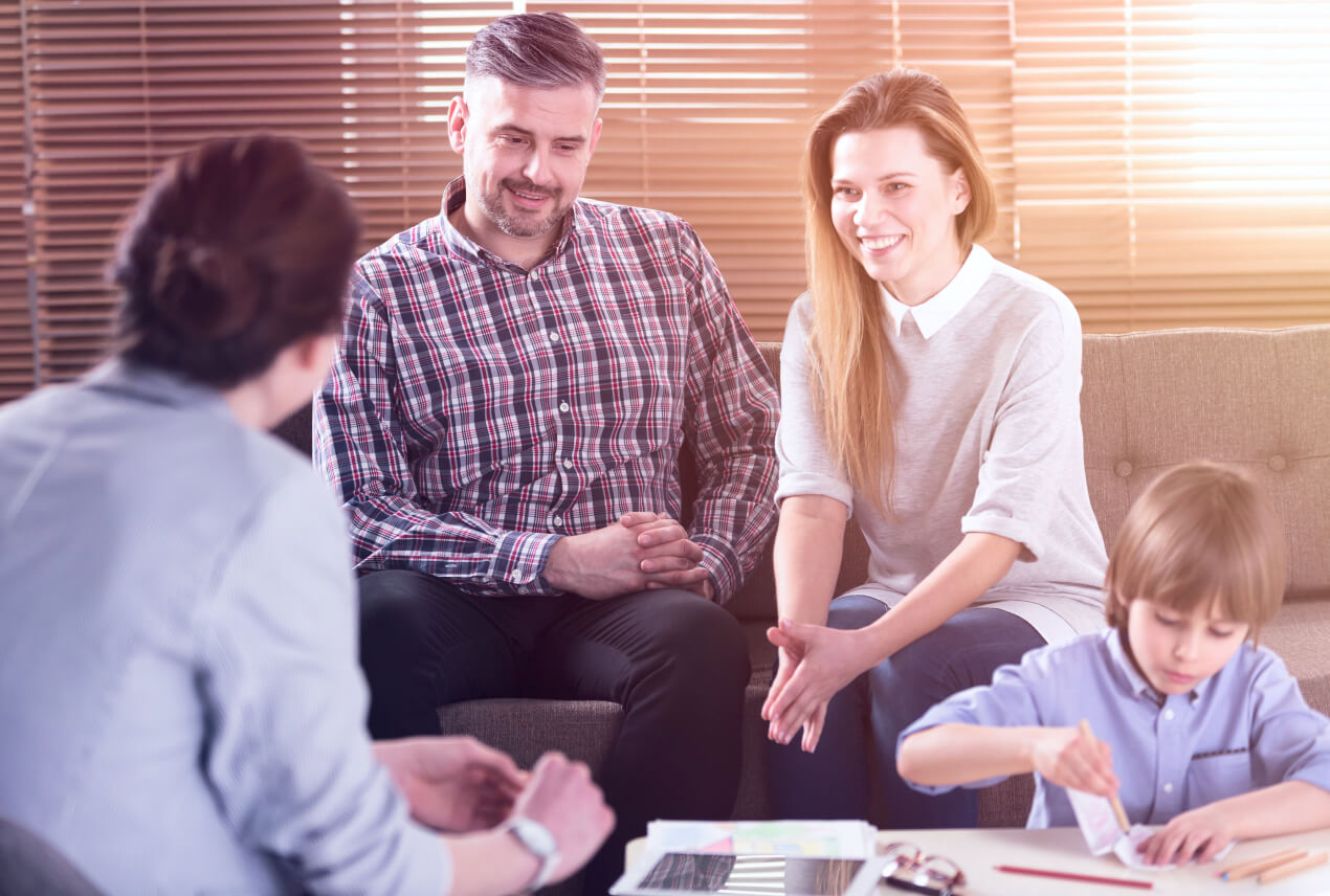 Parents talk to a medical professional while their child plays at a table below them.