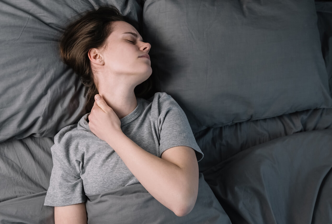 A woman lays in bed holding her neck in pain.