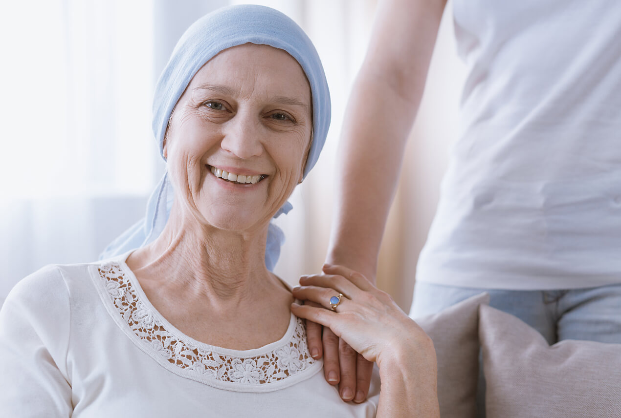 A woman with a blue scarf around her head holds onto a hand placed on her shoulder.