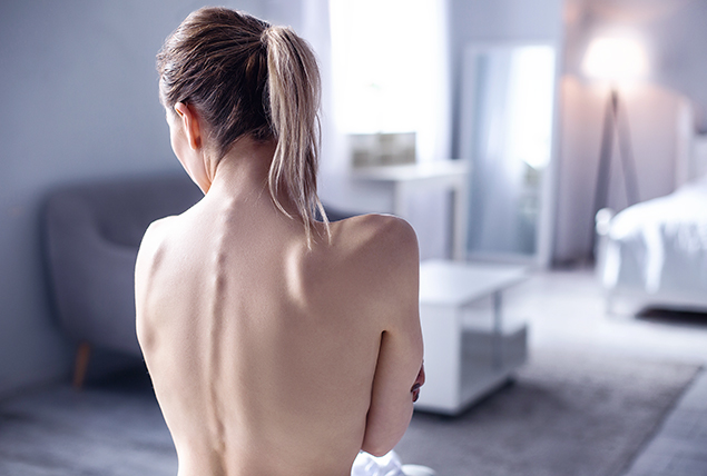 The bare back of a woman displays her spinal cord as she faces away from the camera.