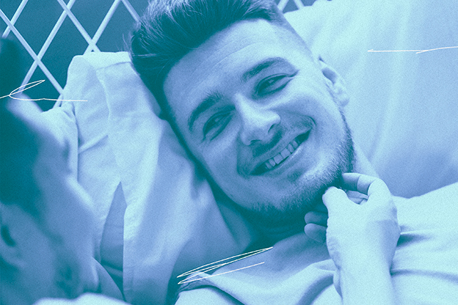A man smiles as he looks at another man while laying down on a pillow.