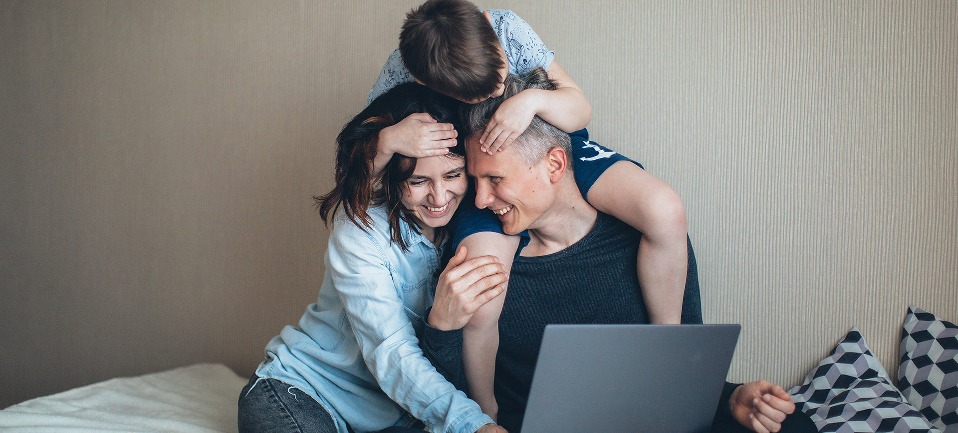Two parents sit around a laptop with a kid climbing on top of them.