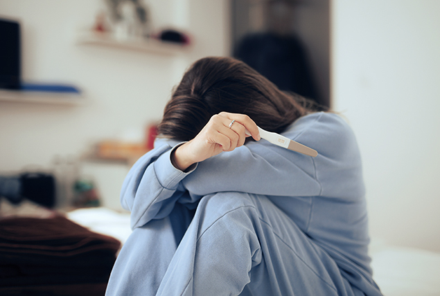 a woman sits and looks upset while holding a pregnancy test