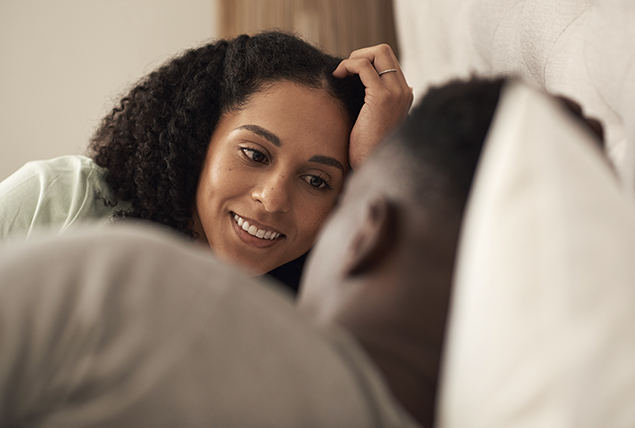 A couple lays down facing each other and talking.