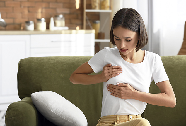 woman in white t shirt does self breast exam while sitting on green couch 