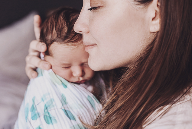 woman holds a baby swaddled in a blue and white blanket close to her face