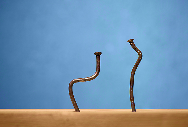 Two nails are bent while stuck in a wooden board against a blue background.
