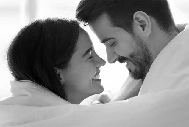 A couple smiles as they embrace under a blanket.
