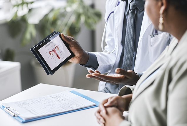 doctors talk as one holds tablet with female reproductive system graphic