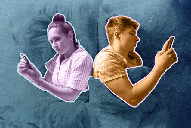 A couple lays in bed together facing opposite directions looking at their phones.