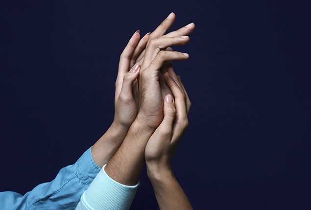 three hands of varying skin tones touching each other romantically on dark navy background
