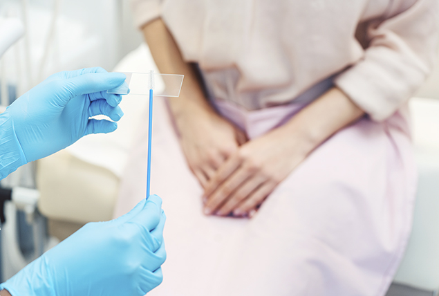 woman in hospitals gown sitting on doctor bed with blue gloved hands swabbing a microscope plate