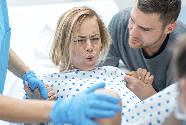 A man stands next to a woman giving birth and holding her hand.