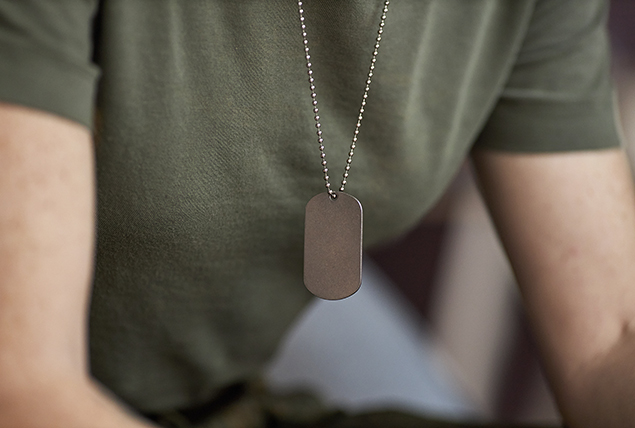 A female military service member leans over as their tag hangs from their neck.