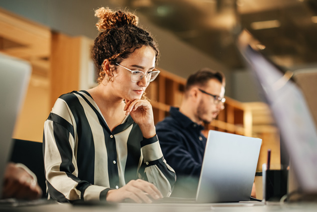 A woman sits next to her coworker looking at her computer.