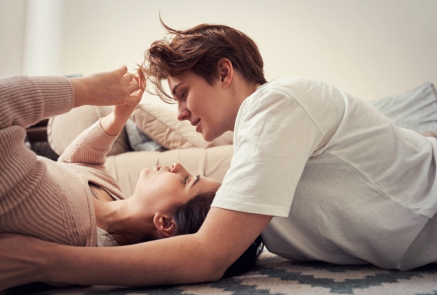 Two queer woman lay down on the floor looking over each other.