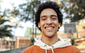 A-teenage-boy-stands-outside-and-smiles-at-the-camera