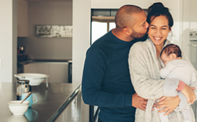 Man-kisses-a-woman-holding-a-baby-in-the-kitchen