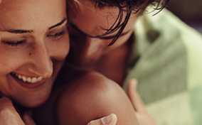 A man nuzzles into a smiling woman's shoulder. 