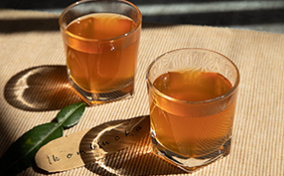 Two glasses of kombucha sit on a table cloth in the sunlight.
