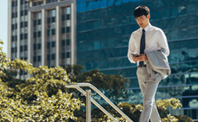 A man in business attire walks in the city while looking at his cellphone.